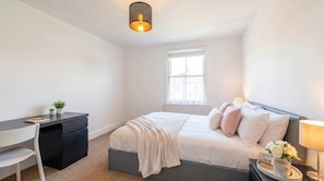 A bedroom with a bed, bedside table, lamp, and a desk with a chair. - Shard View on Terrace 4BR Rare London Station Stay, Close to London Eye, 2 Min walk From Station, Cinematic Scenes for 10 (Greater London)
