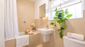 Un baño con bañera, lavamanos, inodoro, espejo y una planta en maceta.