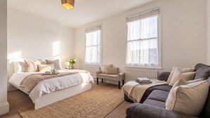 Un dormitorio con cama, sofá, sillón y ventanas amplias.