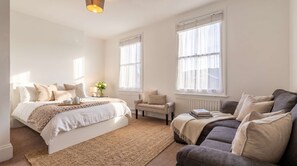 Un dormitorio con cama, sofá, sillón y ventanas amplias.