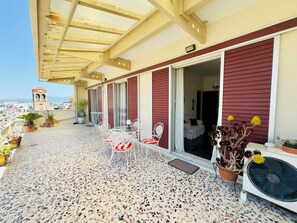 A covered balcony with a terrazzo floor, potted plants, and outdoor furniture.