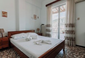 A hotel room with a bed, a nightstand, a lamp, a radiator, and a view of the outdoors through a large window.