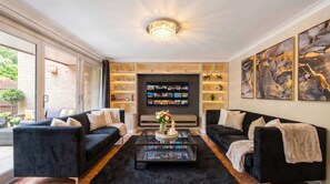 Ein modernes Wohnzimmer mit zwei schwarzen Sofas, einem Glastisch, einem an der Wand montierten Fernseher und dekorativen Regalen.