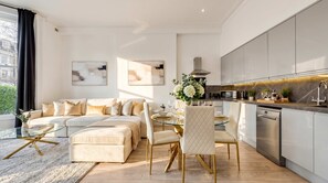 Ein modernes Wohnzimmer mit einer Couch, einem Esstisch und Stühlen, einer Küche mit Geräte sowie Kunstwerken an den Wänden.