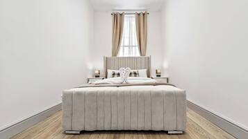 Ein modernes Schlafzimmer mit einem großen Bett, einem Nachttisch, einer Lampe und einem Fenster mit Vorhängen.