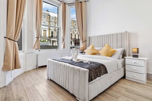 Un dormitorio moderno con una cama grande, una mesita de noche y vistas a edificios a través de la ventana.