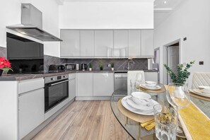 A modern kitchen with white cabinetry, a built-in oven, a microwave, and a coffee maker. - VIRAL Kensignton 2BR Refreshing Dream Home by Station for 6 (Greater London)