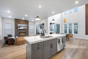 A modern kitchen with a large island, a stone fireplace, and a dining area with a view. - Hot Tub + Fire Pit | Trails + Park City Mtns | Poppy & Pine (Park City)