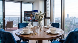 Ein Esstisch für vier Personen, dekoriert mit einem Blumenstrauß, mit einem Fernseher, der Netflix zeigt, und Blick auf die Stadt.
