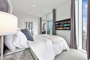 Une chambre d’hôtel moderne avec un grand lit, un téléviseur à écran plat fixé au mur et une vue sur la ville par la fenêtre.