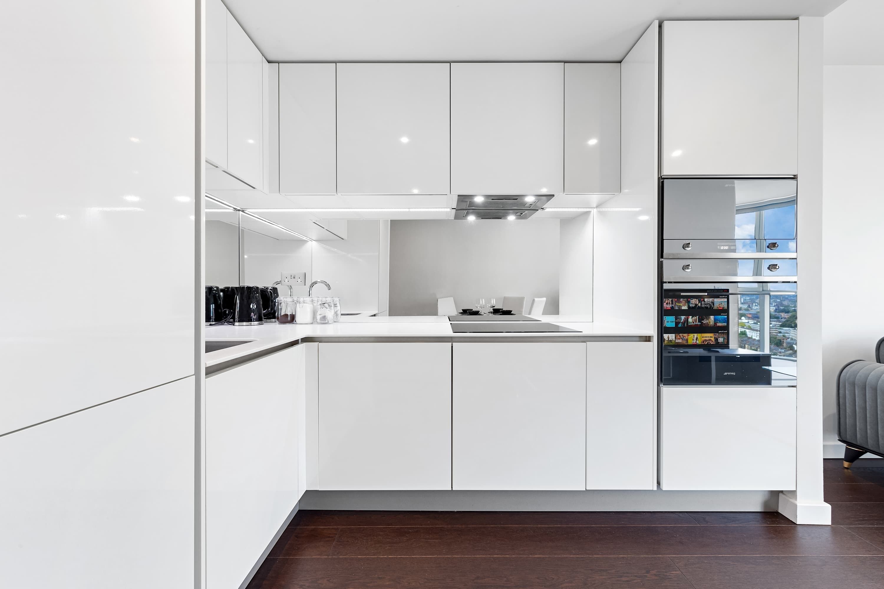 A modern kitchen with white cabinetry, a built-in oven, and a refrigerator with a digital display.