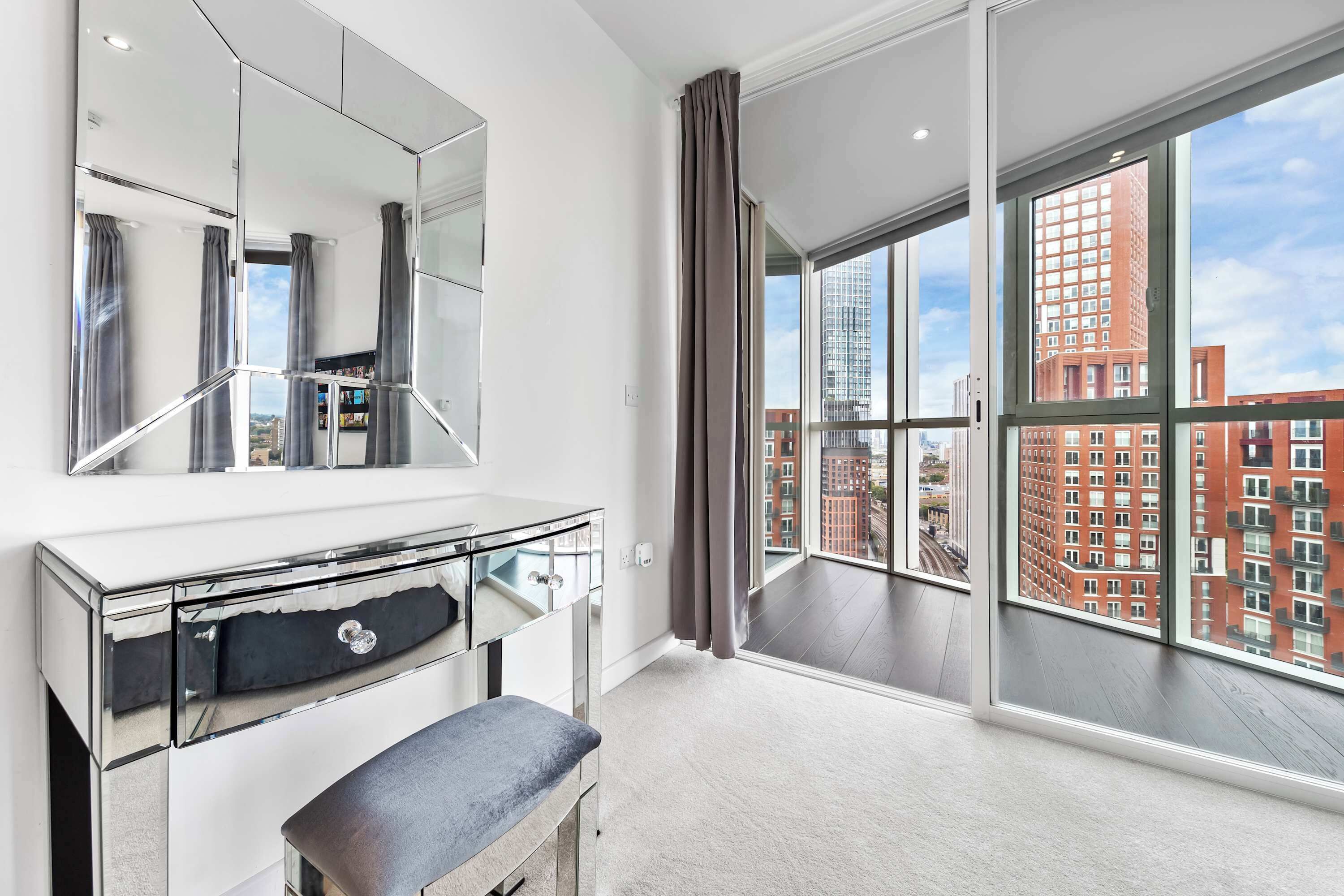 A modern hotel room with a large window, a vanity with a mirror, and a bench.