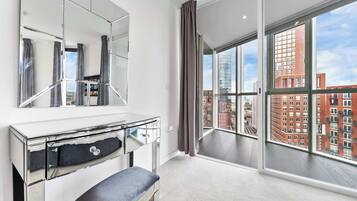 A modern hotel room with a large window, a vanity with a mirror, and a bench.