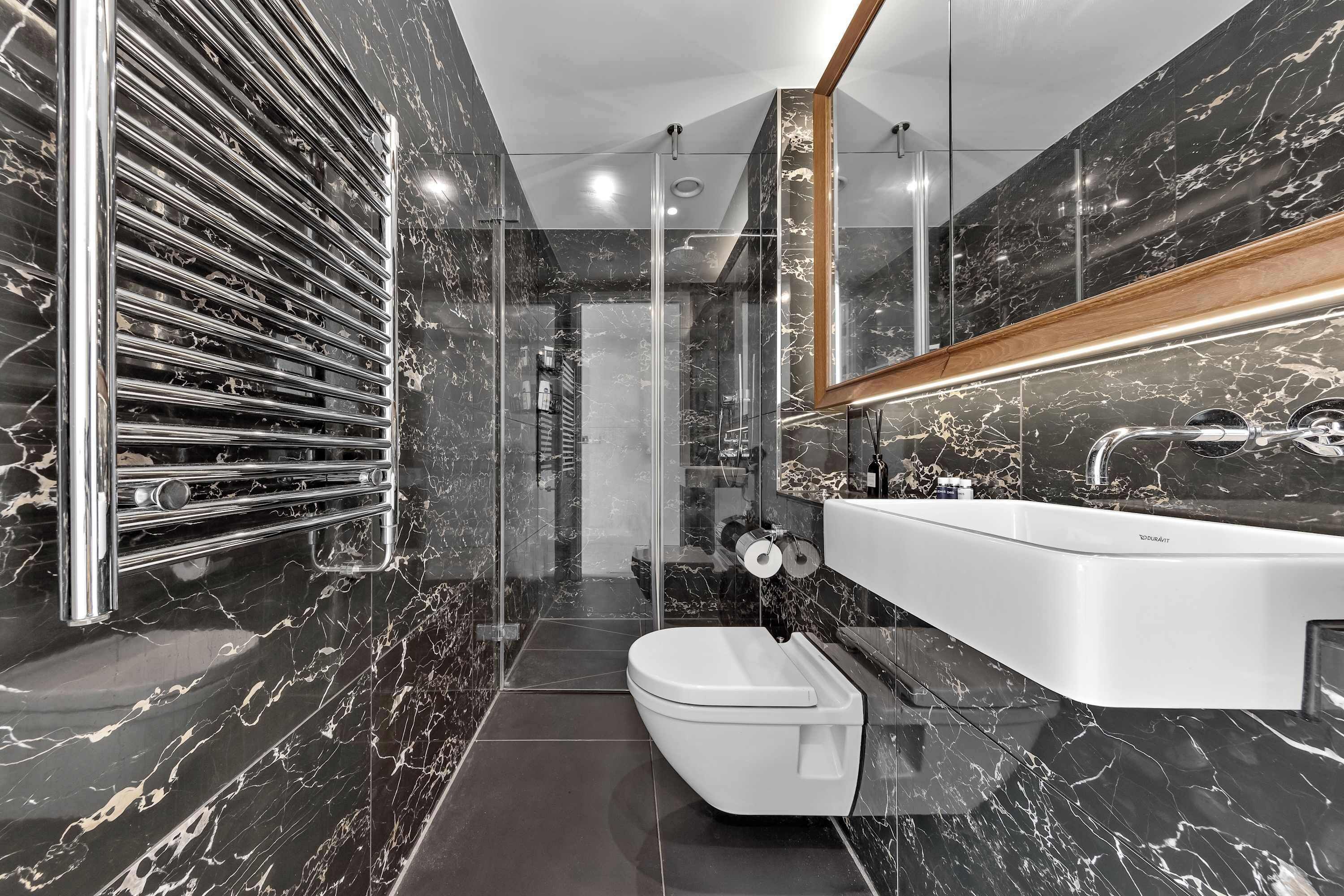 A modern bathroom with a marble backsplash, a glass shower enclosure, and a white sink with a wooden countertop.