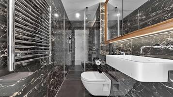 A modern bathroom with a marble backsplash, a glass shower enclosure, and a white sink with a wooden countertop.