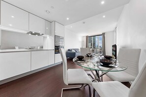 Une cuisine moderne avec des meubles blancs et une table à manger en verre, préparée pour accueillir quatre personnes.