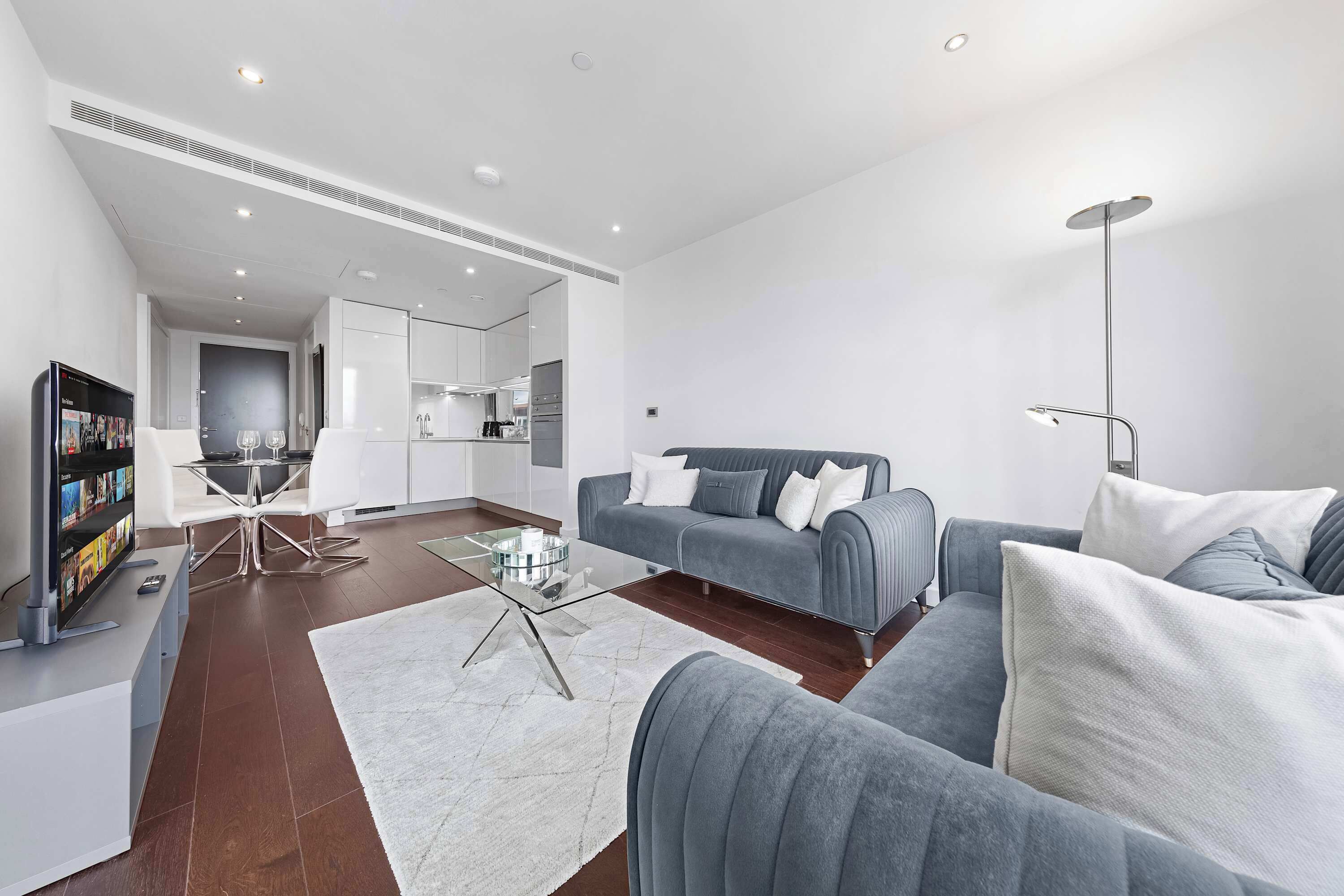 A modern living room with a grey sofa, a glass coffee table, and a flat-screen TV.