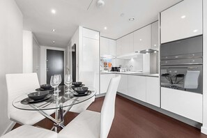 Une cuisine moderne avec des meubles blancs, une table à manger en verre et un four encastré.