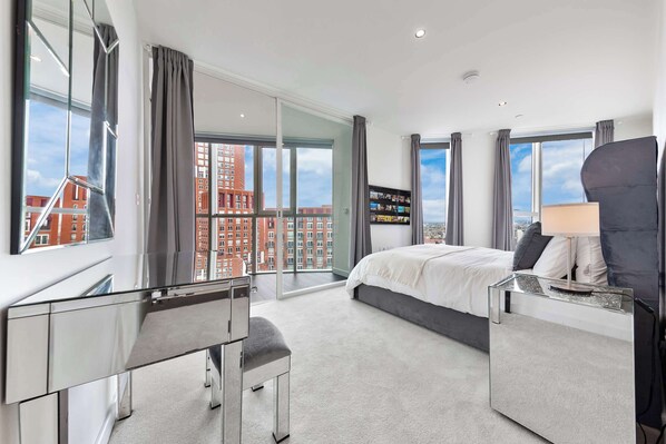 Une chambre d’hôtel moderne, dotée d’un grand lit, d’un bureau et offrant une vue sur le paysage urbain.