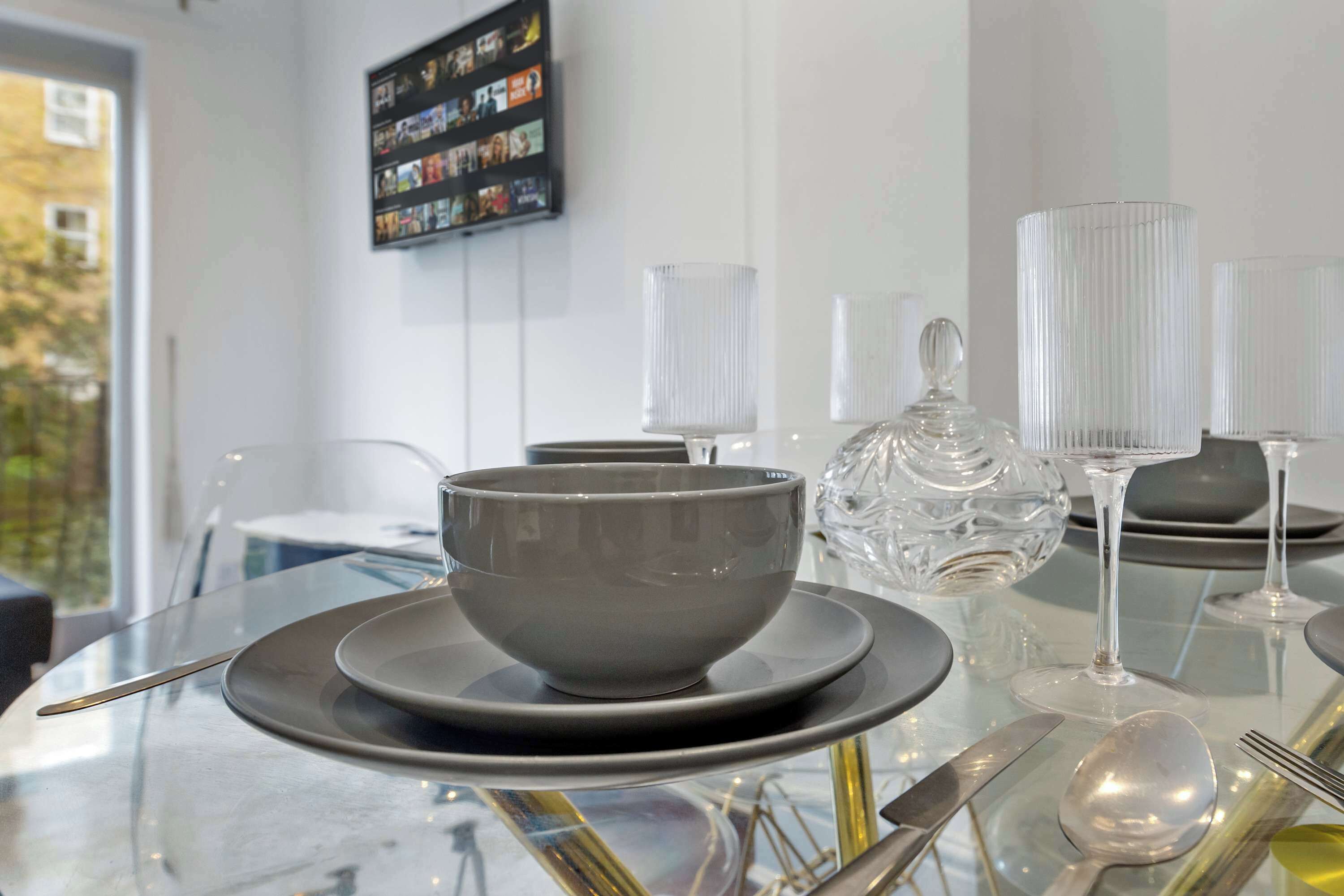 A modern dining table with a bowl, plates, cutlery, and glassware.