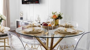 A dining table with clear glass top, gold accents, and a fruit bowl centerpiece. - Notting Hill Neighbour - 2BR Designer Stay (Greater London)