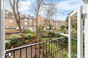 A residential area with brick buildings, a garden with various plants, and a balcony with a metal railing. - Notting Hill Neighbour - 2BR Designer Stay (Greater London)