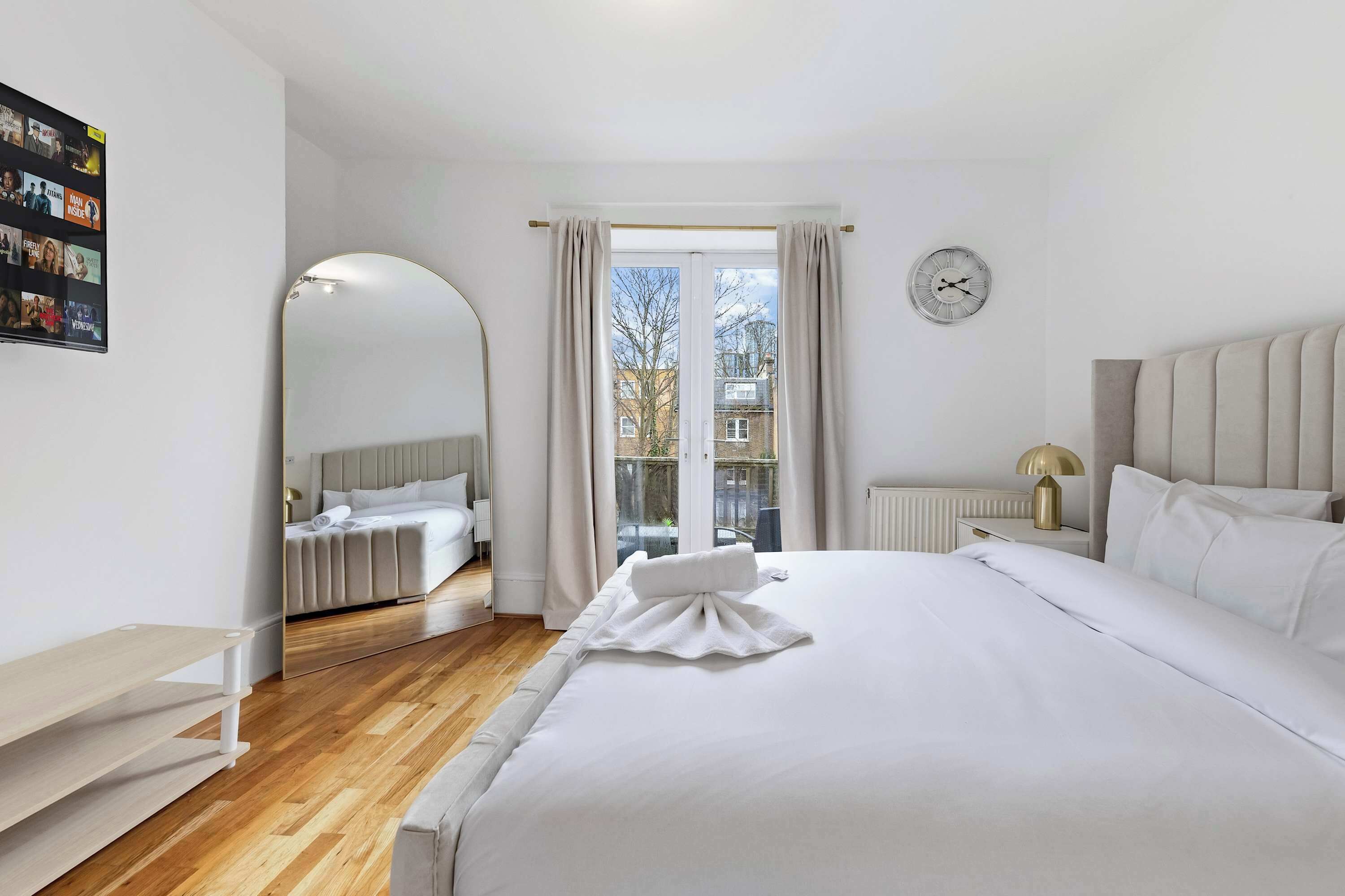 Ein Hotelzimmer mit einem großen Bett, einem Nachttisch mit Lampe, einem Spiegel und Blick nach draußen.