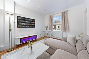 A modern living room with a flat-screen TV, a coffee table, a sofa, and a floor lamp. - Dream Open-View Balcony Apartment for 6 Guests, Moments from Harrods for Beautiful London Nights (Greater London)