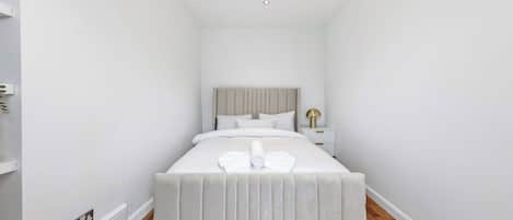 Una habitación de hotel estrecha con una cama, una mesita de noche y una lámpara.