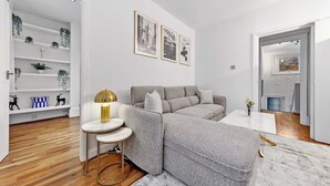 Ett modernt vardagsrum med en grå soffa, ett runt soffbord och en vit vägg med inramade tavlor.
