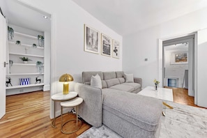 A modern living room with a grey sofa, a round coffee table, and a white wall with framed pictures. - Dream Open-View Balcony Apartment for 6 Guests, Moments from Harrods for Beautiful London Nights (Greater London)