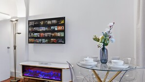 Ett modernt vardagsrum med en platt-TV, en öppen spis, ett matbord med stolar och en tavla som hänger på väggen.