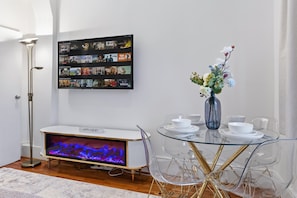 A modern living room with a flat-screen TV, a fireplace, a dining table with chairs, and a wall-mounted picture frame. - Dream Open-View Balcony Apartment for 6 Guests, Moments from Harrods for Beautiful London Nights (Greater London)