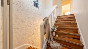 Una escalera con un muro de ladrillo blanco, peldaños de madera, barandilla blanca y un chal de color beige cubriendo la barandilla.