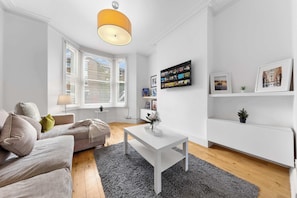 Ein modernes Wohnzimmer mit einer Couch, einem Couchtisch und einem großen Fenster mit Jalousien.