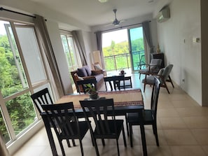 A dining area with a table, chairs, and a view of greenery through large windows.
