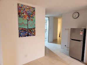 Un pasillo con un refrigerador, un reloj y un cuadro floral colorido en la pared.