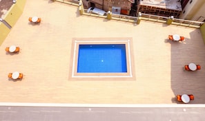 Una piscina en la azotea con suelo de baldosas azules, rodeada de sillas de descanso anaranjadas y blancas.