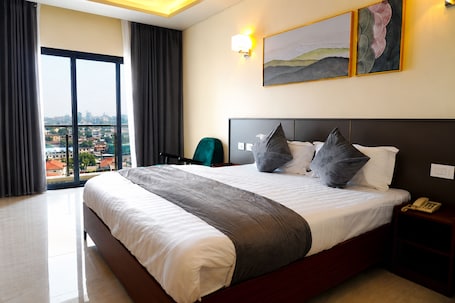 A hotel room with a large bed, a view of the city, a chair, and a nightstand with a phone.. HOTEL PANORAMA