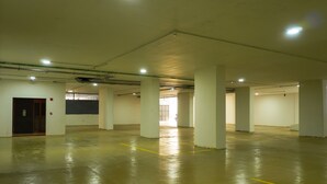 A spacious indoor parking area with concrete floors and white pillars, featuring a door and a visible exit. - HOTEL PANORAMA (Kinshasa)