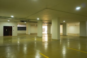 A spacious indoor parking area with concrete floors and white pillars, featuring a door and a visible exit. - HOTEL PANORAMA (Kinshasa)