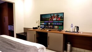 A hotel room with a bed, a desk with a computer, a TV displaying a soccer game, a trash can, and a water bottle. - HOTEL PANORAMA (Kinshasa)