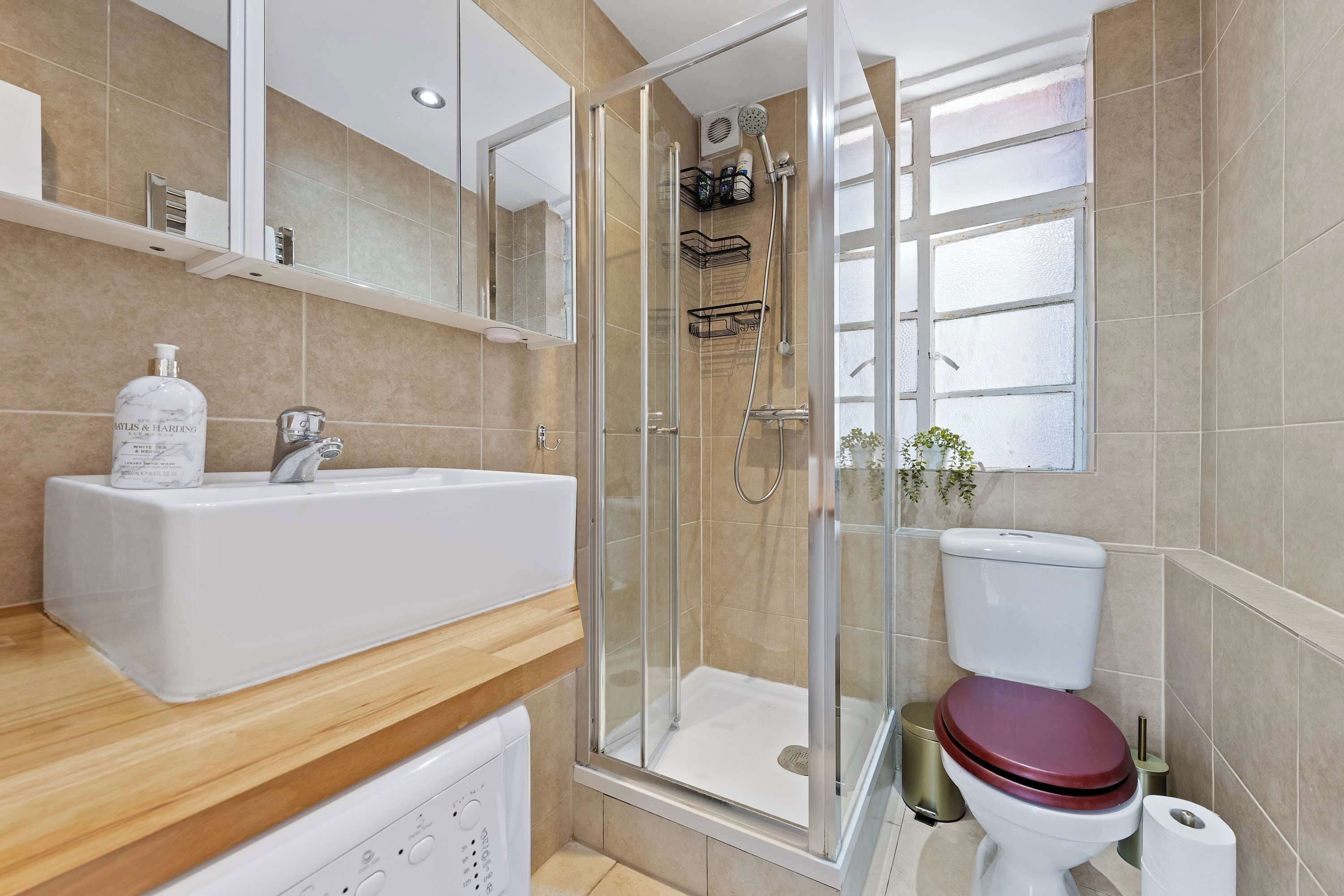 A modern bathroom with a glass-enclosed shower, a white sink, and a toilet with a wooden seat.