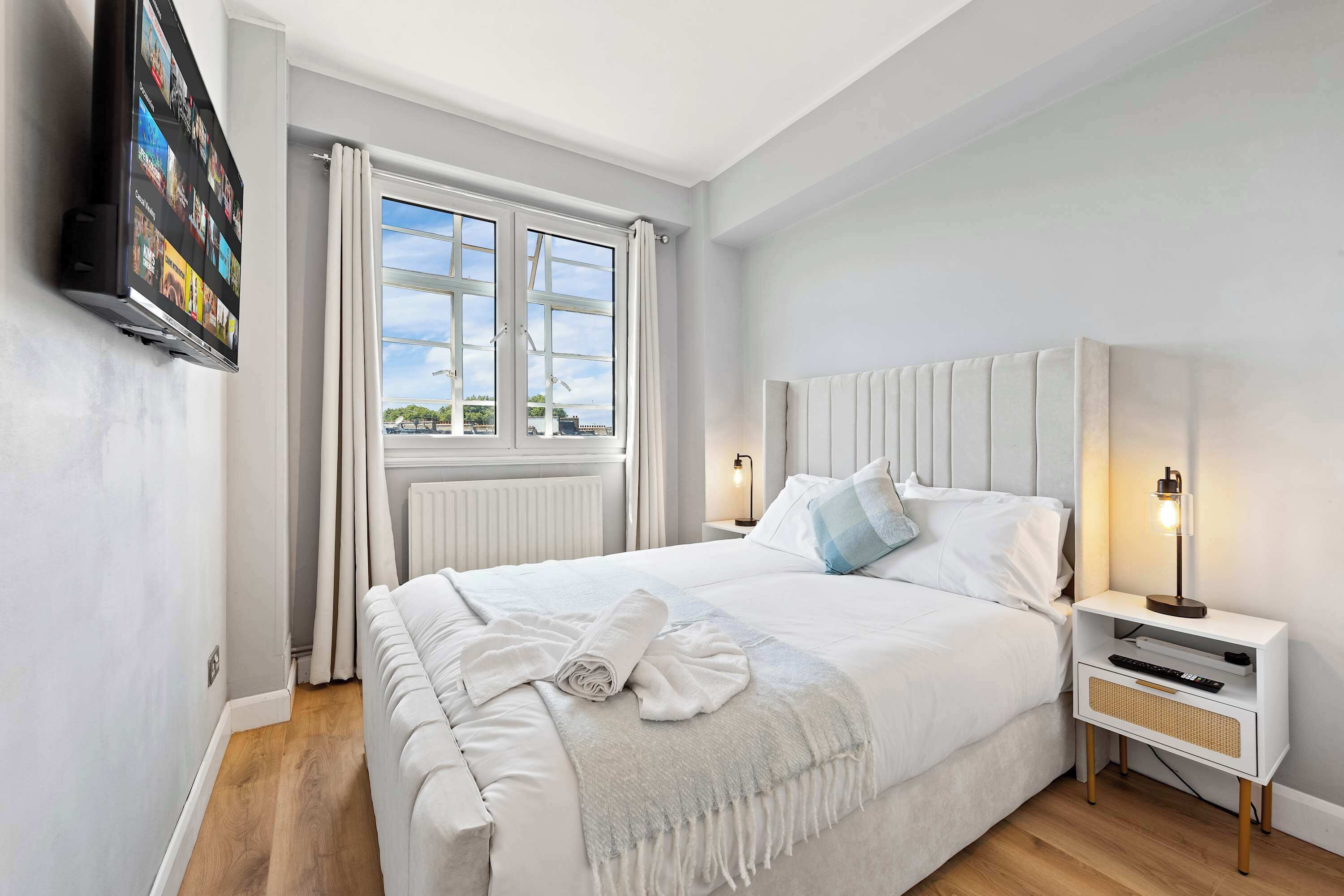 Une chambre à coucher avec un lit, des tables de chevet, une télévision et une fenêtre avec des rideaux.