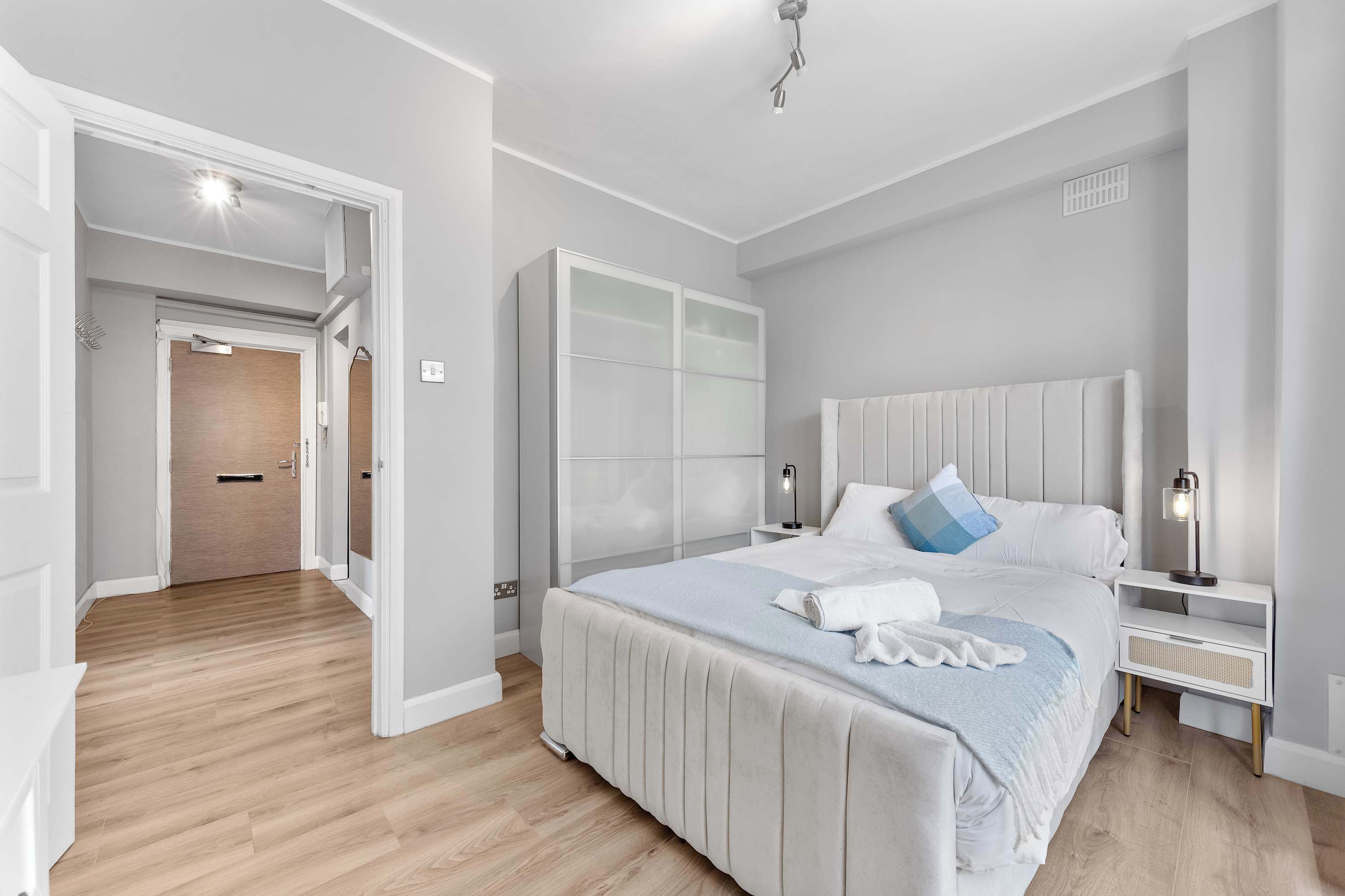 A modern bedroom with a large bed, a wardrobe, and a bathroom visible through an open door.