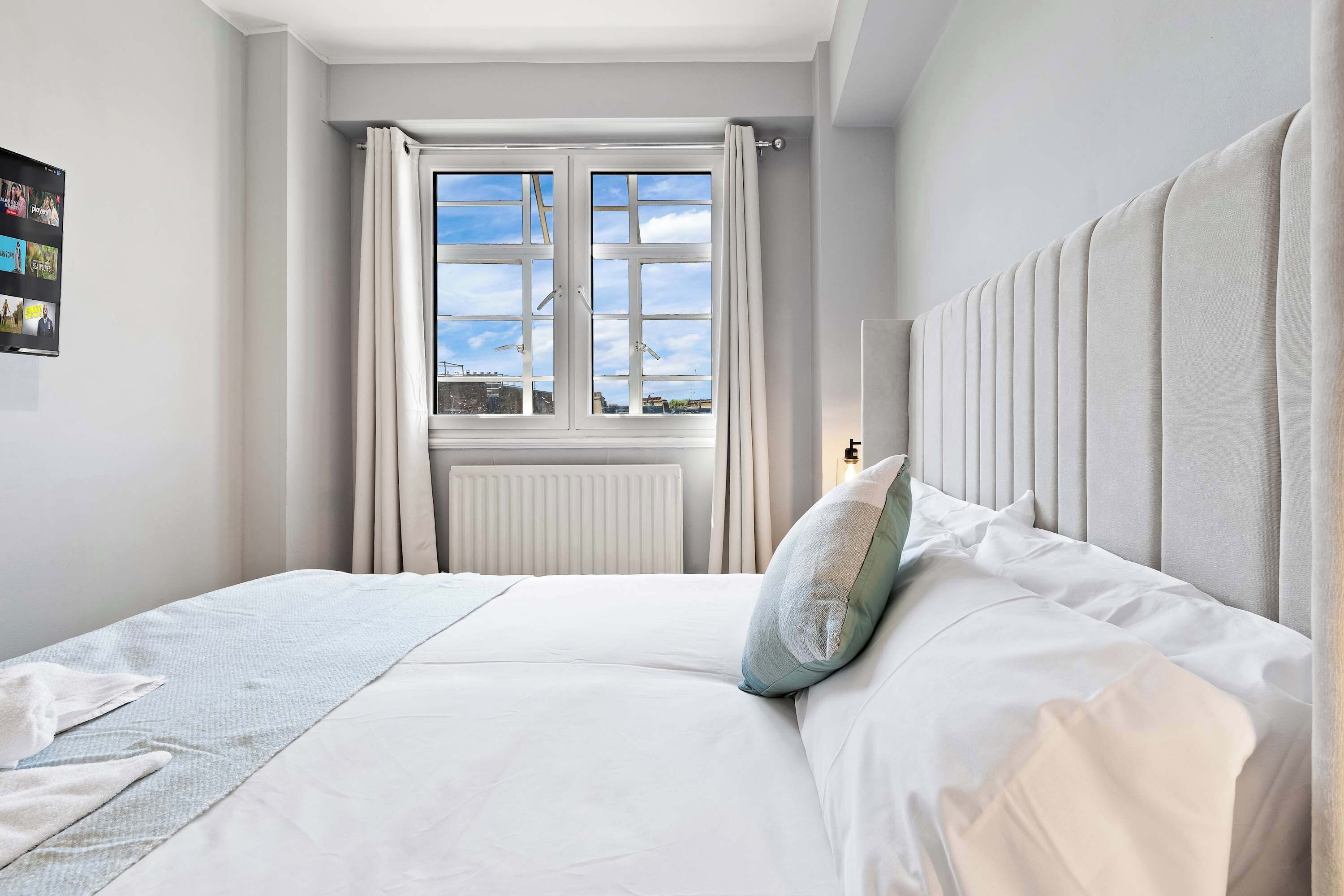 Une chambre d’hôtel avec un grand lit, une vue sur la ville par la fenêtre et un radiateur.