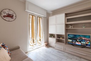 Ein Wohnzimmer mit Sofa, Fernseher der einen Streaming-Dienst anzeigt, einer Uhr und einer Schiebetür.