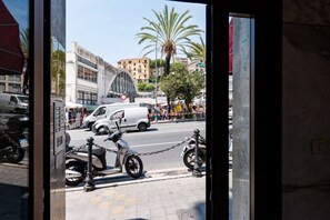 Vista de la calle con scooters estacionados, una camioneta blanca y un edificio con una característica arquitectónica destacada.