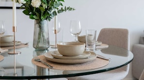 A dining table with a glass top, surrounded by plates, bowls, and cutlery. - London Skyline 1BR with Rooftop, Gym & Shard Views (Greater London)