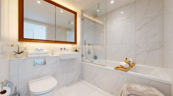 A modern bathroom with a glass-enclosed shower, a white sink, a toilet, and a wooden tray with toiletries. - London Skyline 1BR with Rooftop, Gym & Shard Views (Greater London)